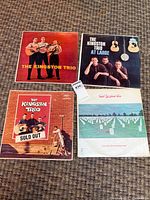 Group shot of all four Kingston Trio album covers on carpet