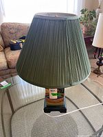 Full view of lamp with green pleated shade on glass table