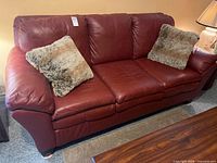 Front view of red leather sofa with two faux fur pillows