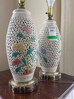 Two white ceramic lattice lamps on table showing floral designs and metal bases