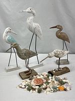 Full group of five carved wood shorebirds on stands with pile of assorted seashells