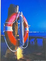 Close view of photograph showing red lifebuoy on piling at night waterfront