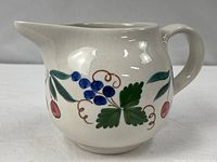 Left front view of hand painted ceramic pitcher showing grape and cherry motif