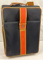 Front view of black suitcase with tan trim and orange strap