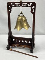 Full view of bell hanging in carved stand with striker in foreground