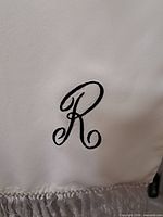 Close-up of embroidered R on ivory satin scarf with fringe