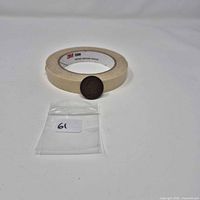Coin leaning against masking tape roll with bag in foreground