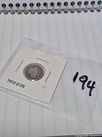 Coin in labelled 2×2 flip on notebook background, obverse visible