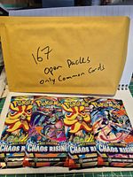 Yellow envelope marked '167 open packs only common cards' alongside several Chaos Rising pack wrappers