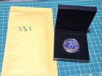 Medallion in capsule inside open black presentation box beside padded envelope