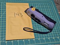 Top view of Polaroid i-Zone camera beside envelope, shows wrist strap and overall wear