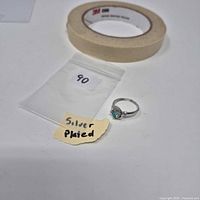 Ring next to bag marked silver plated and tape roll for scale