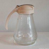 Front view of glass syrup dispenser showing lid, handle and spout