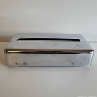 Front view of chrome Kleenex dispenser showing slot and overall form