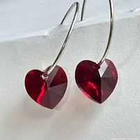Close-up of both earrings showing red heart crystals and silver hoops