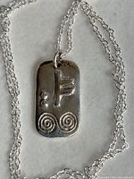front of silver pendant on chain showing rune and spiral design