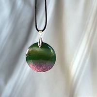 Front view of round green-to-pink druzy agate pendant on black cord