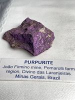 Purpurite specimen on white background with locality label visible