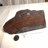 Front view showing banded red jasper and dark hematite layers with coin for scale