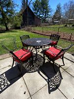 Full view of round cast aluminum table with four matching chairs and red cushions set up on patio