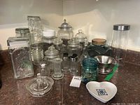 overall lot showing various clear glass jars, shakers, juicer, metal bowls, ceramic heart dish