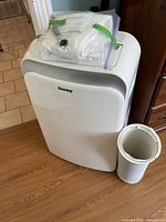 Front view of Danby air conditioner with bagged accessories on top and exhaust hose beside unit