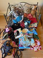 Overall view of lot on metal dog bed showing toys, harnesses, clothing, bowls, packaged items