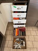 Open drawer stack with trays showing utensils, cutlery piles, cookbooks, oven mitt
