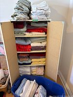 Cabinet shelves with folded towels and blue bin of linens