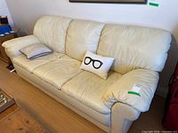 Full view of off-white leather sofa with two accent pillows