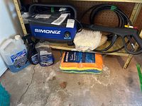 Pressure washer main unit with hose, gun, mitt and towels alongside cleaning fluids