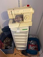Singer sewing machine on plastic drawer tower beside bins