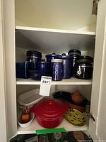 Cupboard view showing blue glass jars, white baking dishes, garlic keeper, red casserole and green plate