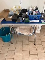 Overall view of items on grooming table including bucket, dog bed, tools and liquids