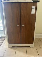 Front view of cabinet showing white frame, brown double doors, round knobs