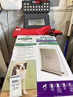 Front of PetSafe pet door box, red pot lifter bag, black folding stool