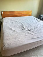 Full view of bed showing sheet-covered Endy mattress and wooden headboard