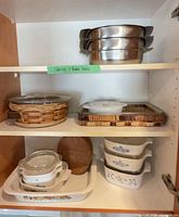 Cabinet shelves showing CorningWare, Pyrex in wicker, wood trays, stainless pans