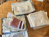 Three boxes containing folded crochet lace tablecloth, embroidered linens, red embroidered napkins and assorted doilies