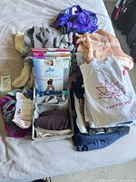 Overview of entire lot on bed showing sweaters, swim top, pantyhose box, stack of tees and socks
