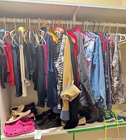 Closet view showing assorted clothing on hangers and multiple pairs of shoes and boots on shelf