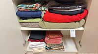 Cabinet shelf with folded quilt, plaid blanket, red, green and black throws and two stacks of assorted fabrics