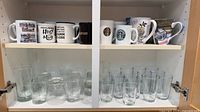 Cupboard overview of mugs on upper shelf and glass tumblers on lower shelf