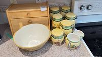 Full lot view with mixing bowl, wooden box and seven ceramic canisters on countertop