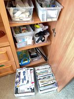 Cabinet with open door showing plastic bins of sewing notions and two file boxes of patterns on floor