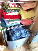 Stacks of assorted folded fabrics on closet shelf showing variety of colors and prints