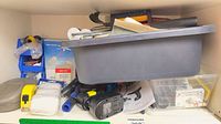 Shelf with gray tub holding drill, battery, tape measure, screws, cloths, parts bins visible