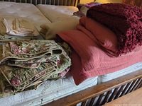 Stack showing floral quilt, coral quilt, red knit throw, beige blanket, cream sheets