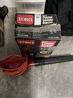 Blower with orange cord attached to black nozzle beside original Toro box