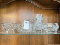 Four crystal pieces on shelf: cylindrical vase, round bowl, two footed bowls
